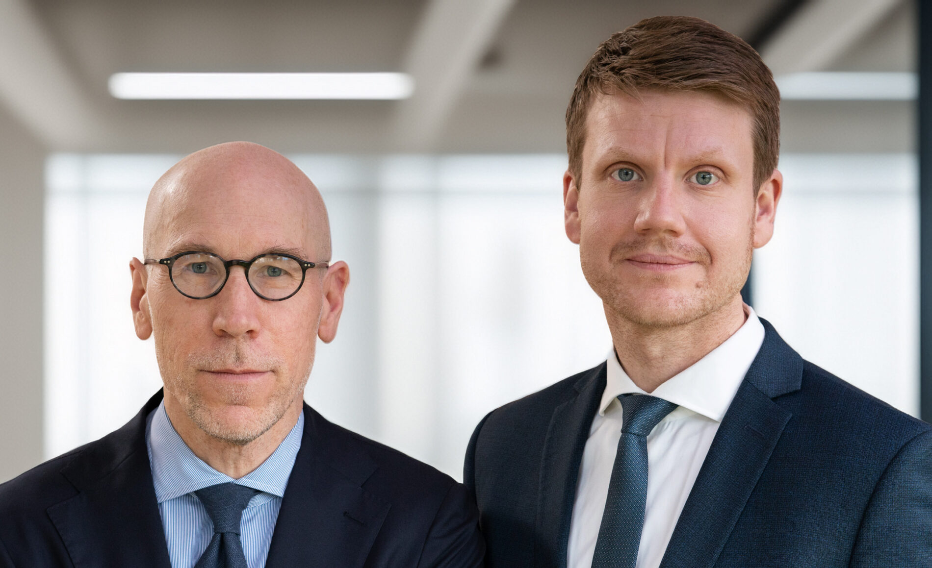 Zwei Notare des Notariats Fruh & Kerstan in Mönchengladbach, im Porträt vor modernem Bürohintergrund